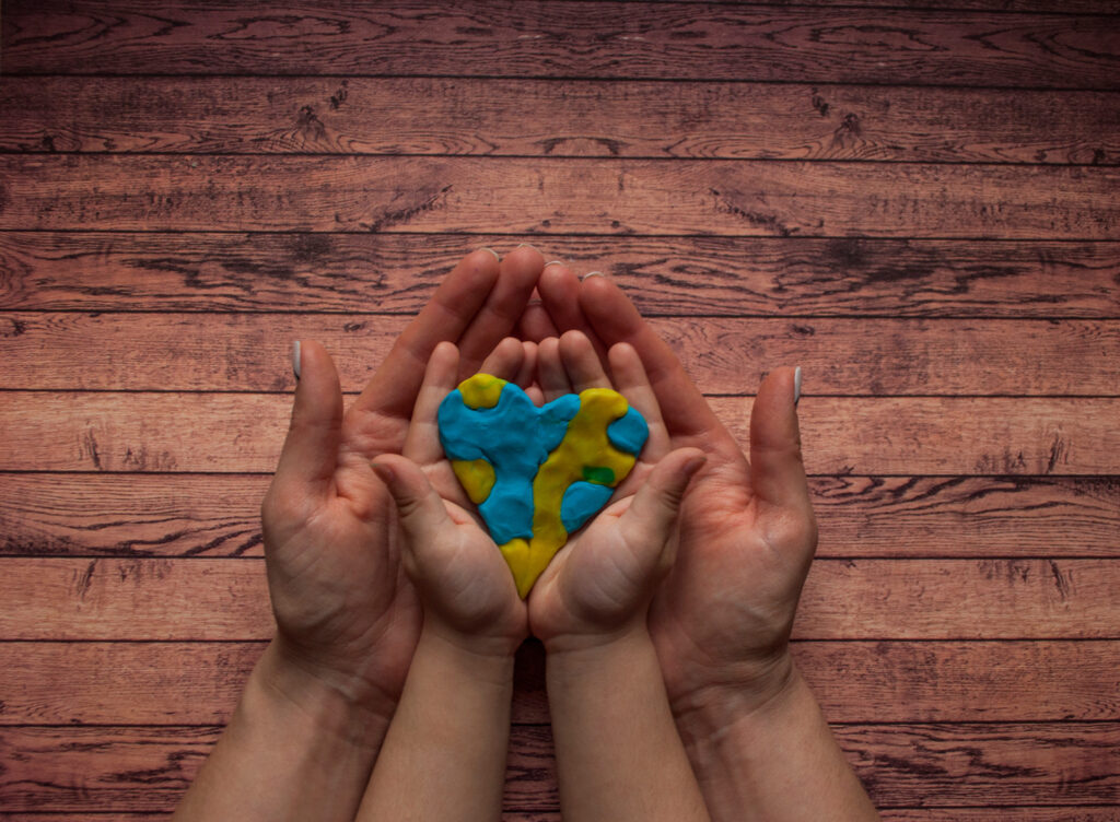 Woman’s and child’s hands holding a heart of blue and yellow col